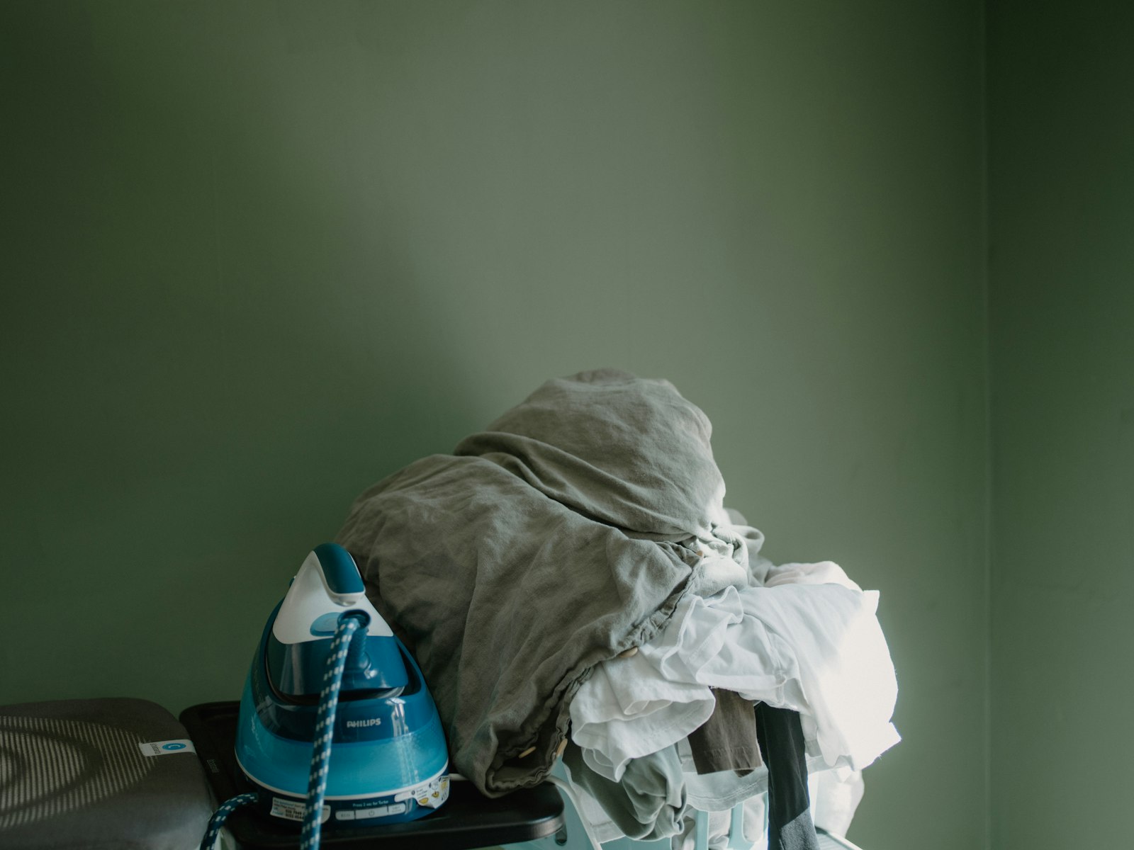 An iron beside a pile of clothes on an ironing board